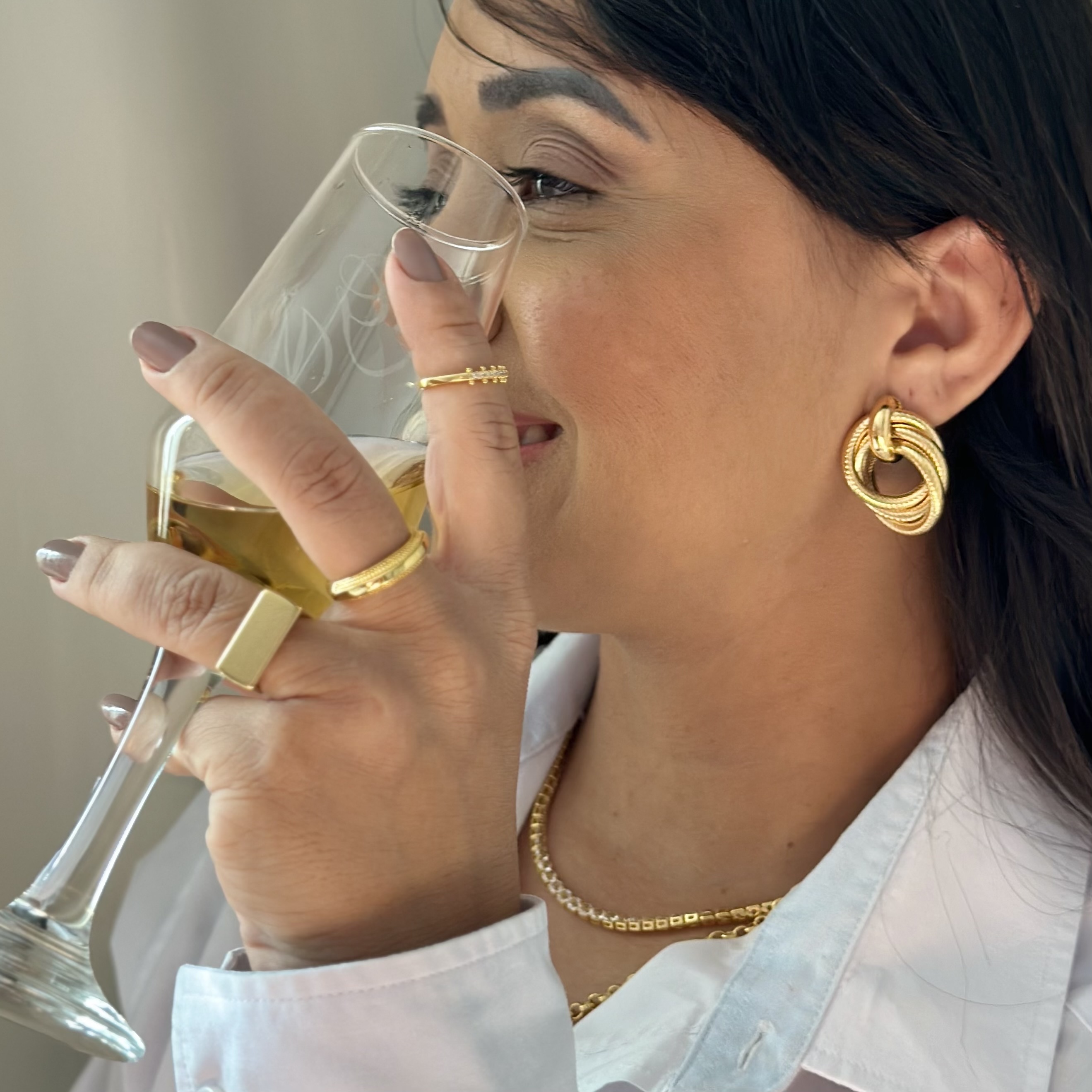 Proprietária da Amaly usando acessórios dourados e segurando uma taça.