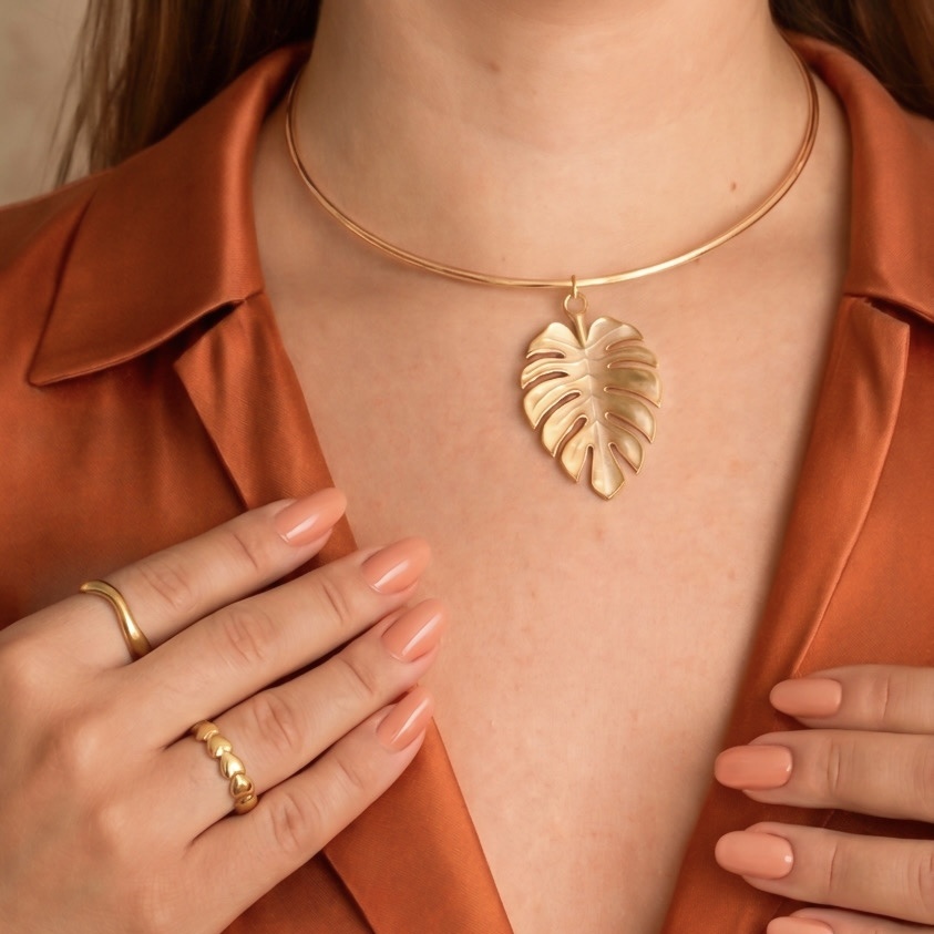 Colar dourado com pingente de folha usado por modelo